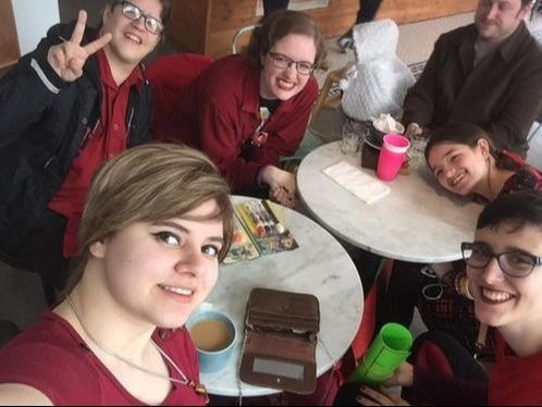 People sitting at tables in a cafe smiling and posing for a group selfie.